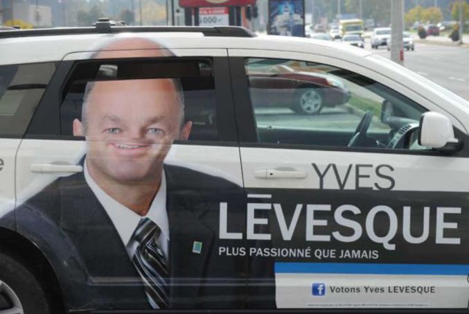 Yves Levesque a eu une bonne idée en faisant sa pub sur des voitures. Seul problème, en ouvrant les vitres, il a tête plus que bizarre! height=